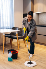 Fototapeta premium People, housework and housekeeping concept - Happy woman or housewife with mop cleaning floor and dancing at home.