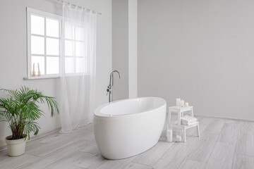 Naklejka na ściany i meble Modern bathtub, houseplant and table with candles in bathroom interior