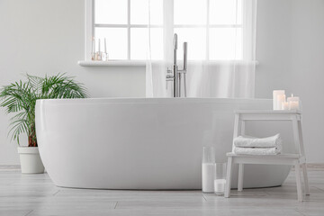 Obraz na płótnie Canvas Modern bathtub, houseplant and table with candles in bathroom interior