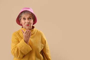 Senior woman in bucket hat blowing kiss on beige background © Pixel-Shot