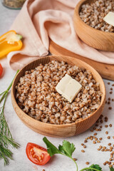 Wooden bowl of tasty buckwheat porridge with butter on grey table
