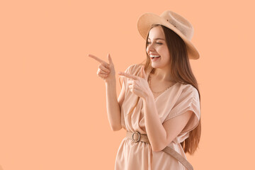 Young woman in hat pointing at something on beige background