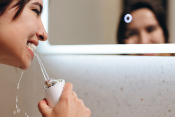 Woman with perfect white smile using portable water flosser or oral irrigator.
