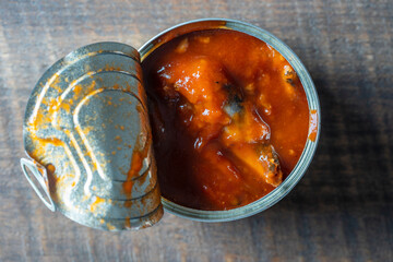 Open canned sprats in tomato sauce on a wooden background, closeup, top view