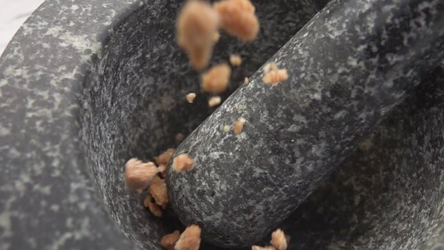 Pieces of brown sugar are falling into the grey stone mortar