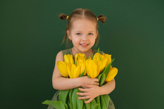 A pretty, comely girl in a green dress is hugging a bouquet of yellow tulips as a gift to her mother. World Women's Day.