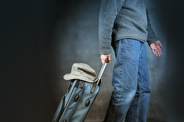 Cut view of man rolling his suitcase at the airport, wearing sweater and jeans