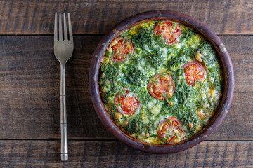 Ceramic bowl with vegetable frittata, simple vegetarian food. Frittata with egg, tomato, pepper, onion, broccoli and cheese on wooden table. Italian egg omelette
