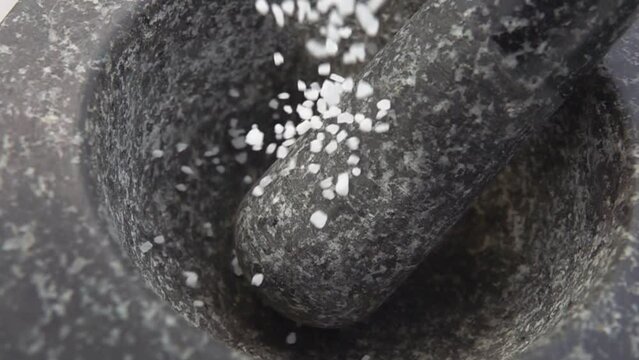 Close-up of the sea salt falling and bouncing in the grey stone mortar