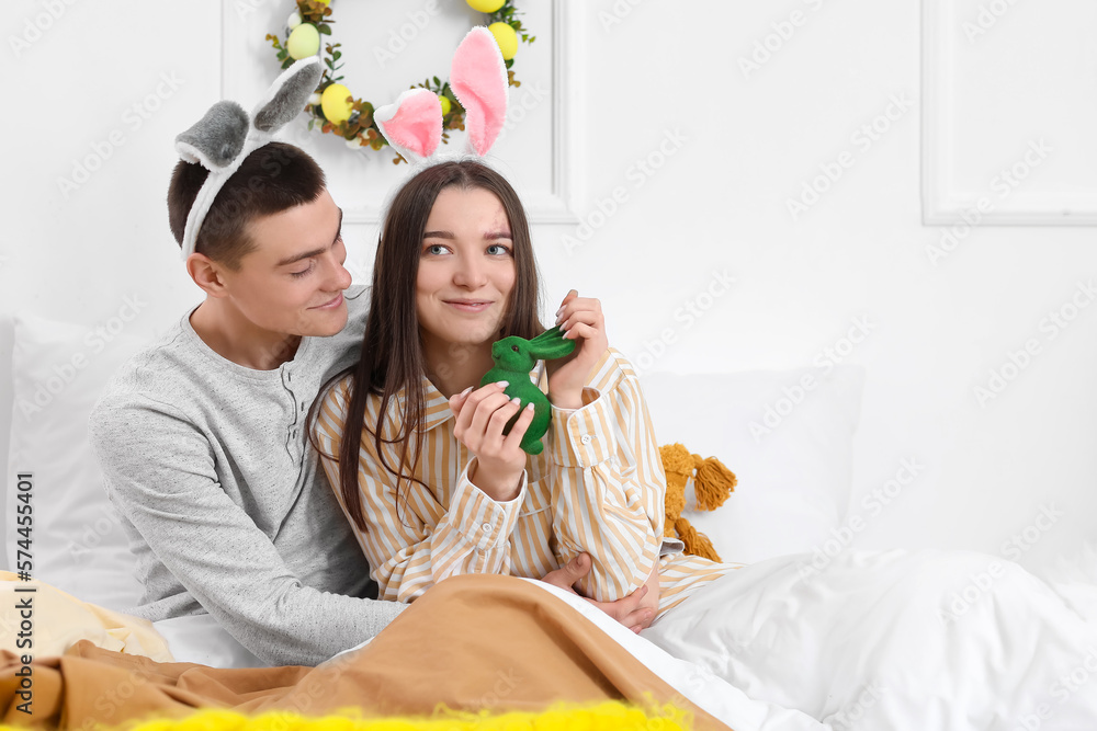 Wall mural happy young couple with bunny ears and easter rabbit in bedroom