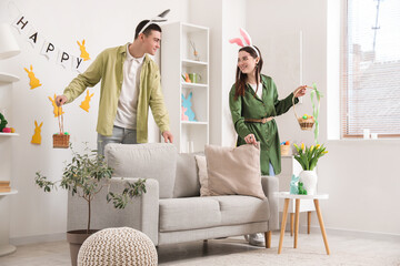 Happy young couple in bunny ears searching for Easter eggs at home
