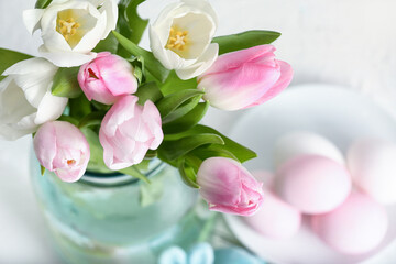 Vase with beautiful tulip flowers and Easter eggs on light background, closeup