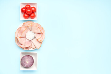 Dishes with slices of tasty ham, sea salt, onion and tomatoes on blue background