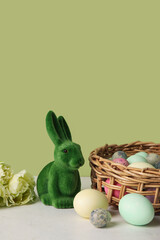 Easter bunny and wicker basket with painted eggs on table against green background