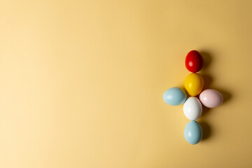 Image of multi coloured easter eggs forming cross with copy space on yellow background
