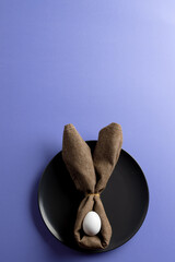 Naklejka premium Image of white easter egg and bunny ears on black plate and copy space on purple background