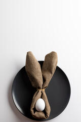 Image of white easter egg and bunny ears on black plate and copy space on white background