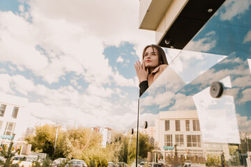 Caucasian young pretty stylish woman standing near business office center glass balcony railing dressed brown trench coat smiling happy outside park, spring autumn season. Brunette hair lady
