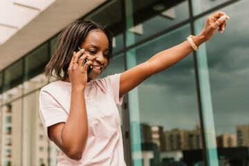 African american woman hold hand phone surfing internet chatting friends colleague call order taxi or food standing talking phone speaking outside street smiling happy positive good mood

