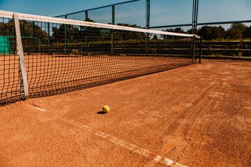 Light orange empty outdoor clay court surface dry grungy ground baseline detail for playing tennis with net in sunny day with yellow green ball, gravel texture background, copy space for text 
 - obrazy, fototapety, plakaty