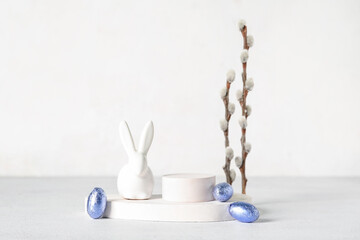 Composition with podiums, chocolate Easter eggs, bunny and willow branches on light background - obrazy, fototapety, plakaty