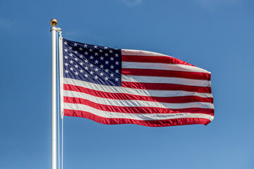 US flag displayed on flagpole with clouds background on a breezy day