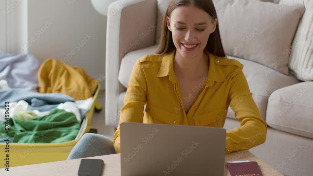 Wall mural Work from everywhere. Young happy woman freelancer typing on laptop at hotel room, working on vacation near luggage