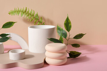 Plaster podiums with ficus and fern branches on pink table against beige background