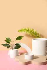Plaster podiums with ficus and fern branches on pink table against beige background