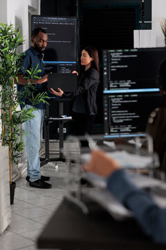 Diverse team of software programmers analyzing html code on wall screen tv, using digital gadget and working with artficial intelligence. Coders parsing cloud computing project with big data.