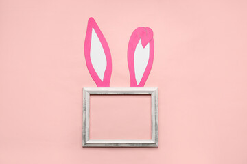 Paper bunny ears and blank wooden frame on pink background