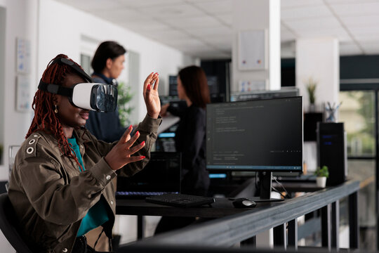 African american system engineer wearing virtual reality goggles working to develop security program in it big data office, software developer with vr headset coding html script with database.