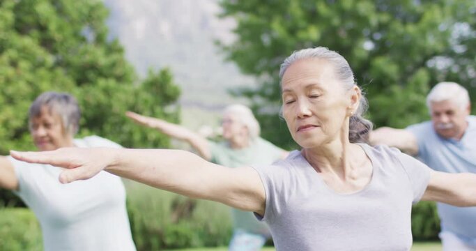 Smiling senior asian woman practicing yoga with diverse senior group in garden, slow motion