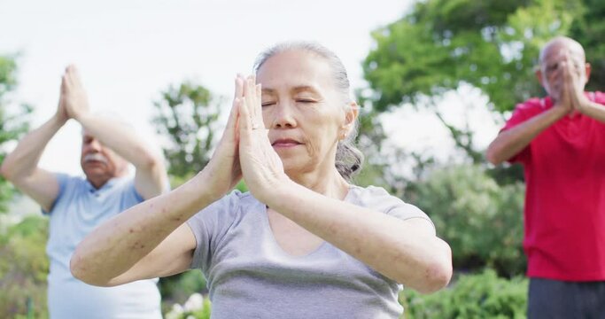 Senior asian woman practicing yoga meditation with diverse senior group in garden, slow motion