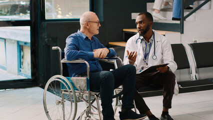 African american doctor doing consultation with old man in wheelchair, filling in medical report...