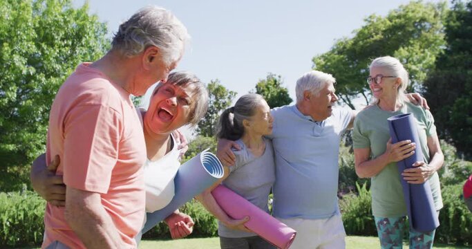 Diverse group of happy male and female seniors talking after exercising in sunny garden, slow motion