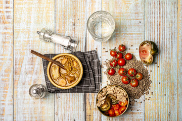 Still life with traditional lentil stew in a wooden bowl and tuna and tomato salad in a golden bowl on a light wooden table - obrazy, fototapety, plakaty