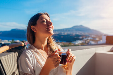 Woman relaxing on hotel terrace drinking morning coffee enjoying Santorini mountain landscape. Breakfast with view - obrazy, fototapety, plakaty