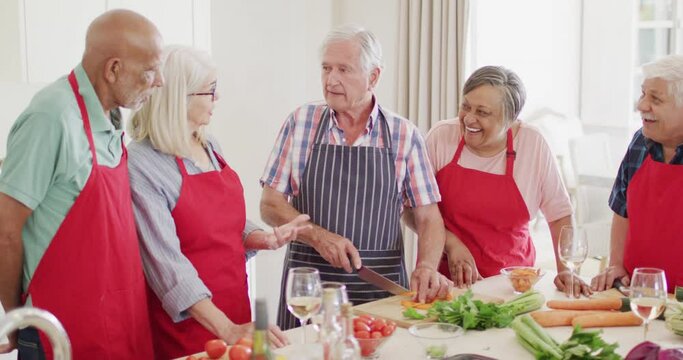 Happy group of diverse senior male and female friends preparing food talking in kitchen, slow motion