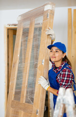 Latin woman in overall working on home improvement in apartment, carrying new wooden door.