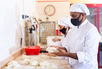 Man and woman in protective mask prepare bread in the kitchen of the bakery