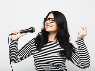 Young curvy woman singer with a microphone over light grey background