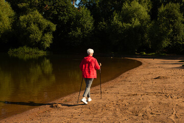 Sporty senior woman trains endurance while Nordic walking in nature