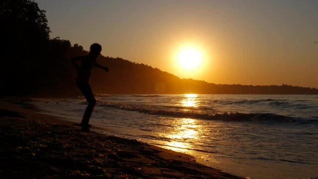 Jumping teen silhouettes on bay. A girl silhouette run and jump on the sandy beach against nightfall sky.