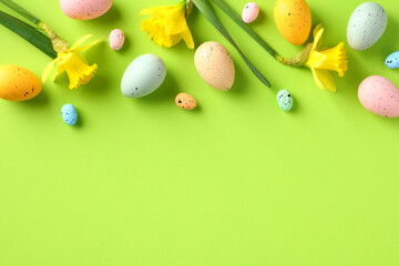 Happy Easter frame top border made of colorful Easter eggs and yellow spring flowers on green table. Easter greeting card template, banner design. Flat lay, top view, copy space.