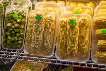 Yellow corn on the cob and green okra wrapped in plastic on a shelf at the Municipal Market in...