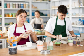 Fototapeta premium Young woman and young man sculpting ceramic product in workshop