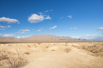 Desert landscape with mountain background and blue sky with white clouds
