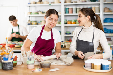 Two young women in apron modeling clay pottery in workshop