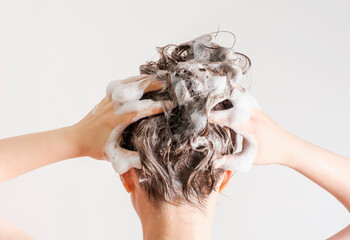 A girl washes her hair with shampoo on white background, back view. - obrazy, fototapety, plakaty